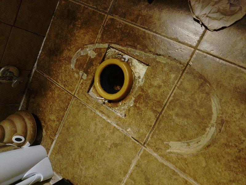 Provided estimate for complete toilet replacement in bathroom showing extensive water damage and deterioration around floor drain area. Assessment revealed significant water staining on ceramic tile floor with discoloration patterns indicating prolonged leakage issues, likely from failed wax ring seal. Inspection documented existing toilet installation with chrome flexible supply line and wall-mounted shut-off valve. Customer requested revised estimate to include additional scope items beyond standard toilet replacement to address underlying water damage concerns.