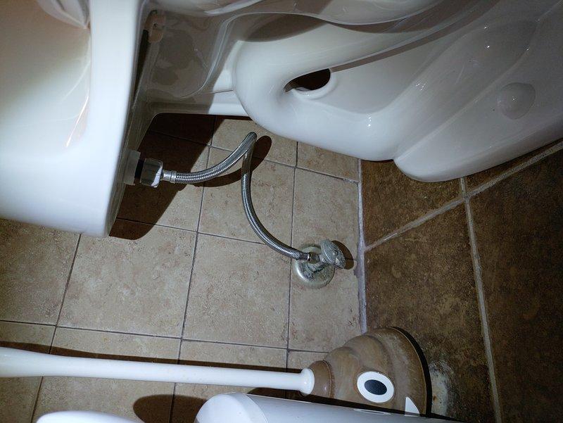 Provided estimate for complete toilet replacement in bathroom showing extensive water damage and deterioration around floor drain area. Assessment revealed significant water staining on ceramic tile floor with discoloration patterns indicating prolonged leakage issues, likely from failed wax ring seal. Inspection documented existing toilet installation with chrome flexible supply line and wall-mounted shut-off valve. Customer requested revised estimate to include additional scope items beyond standard toilet replacement to address underlying water damage concerns.