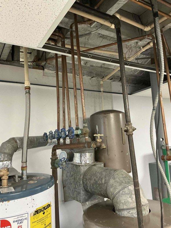 Conducted estimate for aging hydronic boiler system in basement utility area. System exhibits significant age-related deterioration with weathered components, corroded piping, and outdated infrastructure requiring complete replacement. Documented existing configuration including expansion tank, manifold with multiple zone valves, copper distribution piping, and primary heating unit for comprehensive replacement proposal.