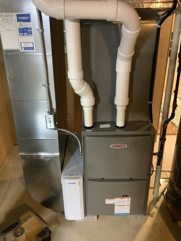 Completed full HVAC system installation including a new Lennox high-efficiency furnace in the basement utility area and matching Lennox outdoor condensing unit. The indoor installation features proper PVC venting configuration with dual vertical exhaust/intake pipes, integrated Aprilaire air quality equipment with control module and connecting conduit, and appropriate placement on the concrete floor with access to existing ductwork. The outdoor unit was positioned on a protective pad against the home's exterior with adequate clearance from the foundation and landscaping, ensuring proper airflow and serviceability. All components were installed per manufacturer specifications with proper electrical connections, refrigerant lines, and condensate drainage, resulting in a complete heating and cooling system ready for operation.