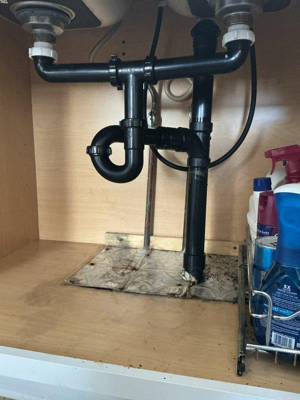 Replaced deteriorated drain assembly under kitchen double sink with new black PVC P-trap configuration and installed air admittance valve (AAV) to resolve drainage issues and prevent sewer gas infiltration. Removed existing chrome compression fittings and corroded piping, installed new drain lines with proper venting, and tested system for leaks and proper flow upon completion.