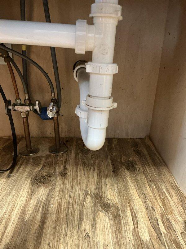 Responded to service call for clogged kitchen sink in 20-year-old residence. Upon arrival, inspected stainless steel double-bowl sink with visible standing water and soap residue in both basins indicating drainage issues. Accessed cabinet beneath sink and examined plumbing assembly including P-trap, drain lines, and supply connections. Cleared blockage from drain system restoring proper water flow through both sink bowls. Verified P-trap and all PVC connections were secure with no leaks present. Tested drainage by running water through both basins to confirm complete resolution of clog. All plumbing components left in proper working condition.