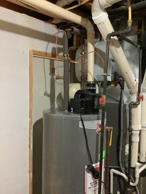 Responded to no hot water complaint at 27-year-old residence with existing tanked water heater system. Upon arrival, assessed Rheem residential water heater unit and associated plumbing infrastructure including expansion tank, copper supply lines, shut-off valves, and circulating pump assembly. Inspected all connections, electrical components, and safety labels for proper operation and code compliance. Documented existing installation showing water heater with integrated expansion tank, PVC venting system, copper water lines with red-handled ball valves, and recirculation pump mounted at top of unit. Verified all plumbing connections, valve operations, and system components. Photographed complete installation for service records showing proper configuration of hot and cold water lines, expansion tank mounting, electrical connections, and venting arrangement in basement mechanical room.