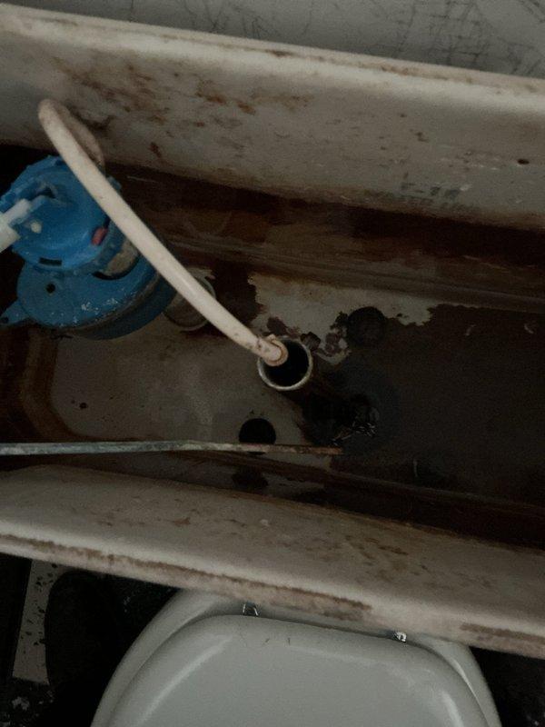 Responded to a multi-issue plumbing service call at a 60-year-old residential property addressing clogged drain, water leak, and toilet repair. Upon arrival, inspected utility sink with significant mineral buildup and staining around drain assembly and faucet fixtures. Cleared obstruction from drain line using appropriate tools and verified proper water flow. Examined plumbing components in confined access area beneath sink, identifying deteriorated conditions including rust staining, water damage, and corrosion on surrounding surfaces. Inspected white PVC piping connections and joints for integrity, noting the presence of a blue valve assembly in the system. Addressed leak source by tightening connections and assessing condition of aging pipes showing signs of prolonged moisture exposure. Performed toilet repair by examining tank components and making necessary adjustments to restore proper function. Tested all fixtures following repairs to ensure proper operation and drainage. Docume