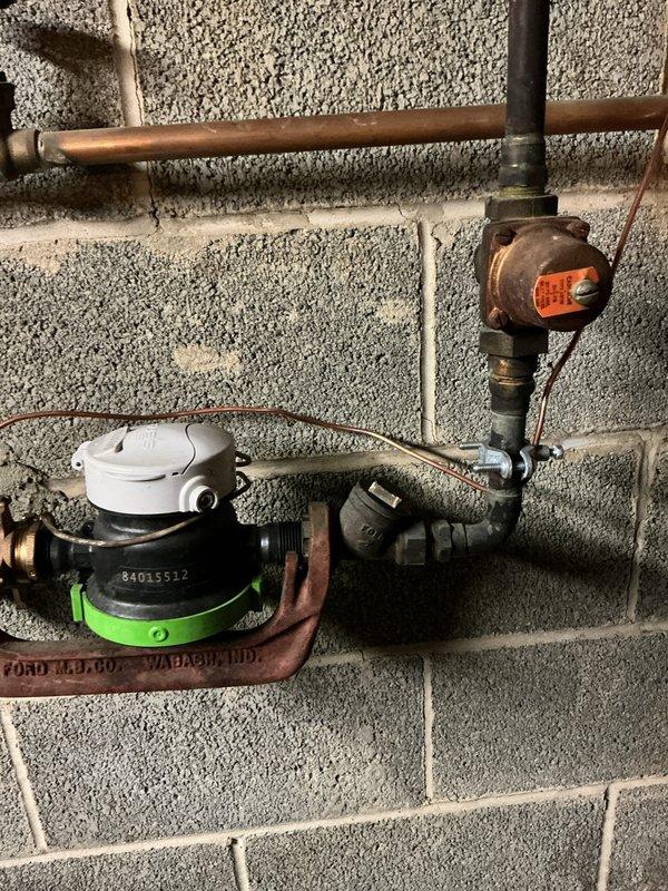 Responded to service call for malfunctioning pressure regulator valve and thermal expansion tank in 66-year-old residential property. Upon arrival, inspected existing plumbing assembly mounted on basement utility wall, noting significant age-related corrosion and oxidation on copper piping and valve components. Water meter assembly and associated gate valves showed weathering consistent with original installation. Evaluated pressure regulation system and thermal expansion tank functionality, documented existing conditions through photography for service records. Assessed copper pipe loop configuration and connection points to determine extent of component degradation and system performance issues affecting household water pressure regulation.