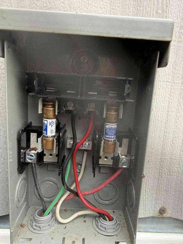 Completed MVP cooling visit and preventive maintenance inspection. Documented electrical disconnect panel showing operational fuse assembly with visible age-related corrosion on internal components and hardware, though all connections remain secure. Inspected condenser coil fins which are in clean condition with proper airflow clearance and no significant debris accumulation or damage present.