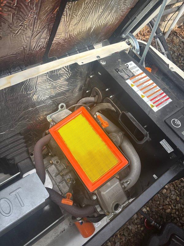 Responded to service call for 7-year-old Generac natural gas generator displaying battery check warning message. Performed diagnostic inspection of unit, verified operational status with green indicator light illuminated, and assessed battery condition and charging system. Documented equipment condition with photos showing outdoor installation on gravel pad with visible weathering on exterior housing.