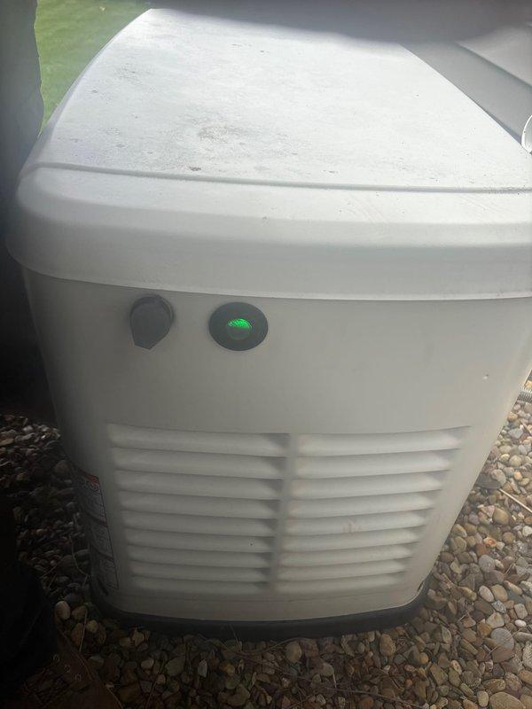 Responded to service call for 7-year-old Generac natural gas generator displaying battery check warning message. Performed diagnostic inspection of unit, verified operational status with green indicator light illuminated, and assessed battery condition and charging system. Documented equipment condition with photos showing outdoor installation on gravel pad with visible weathering on exterior housing.