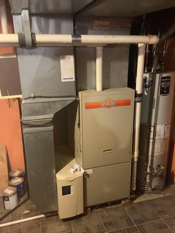 Completed installation of a 90% efficiency furnace and air conditioning system at residential property. New Pulse-branded furnace unit was installed in the basement mechanical room with proper venting using white PVC piping, and outdoor AC condenser unit with beige cabinet and horizontal louvers was positioned on concrete paver patio against exterior of home with appropriate electrical connections and clearances maintained.