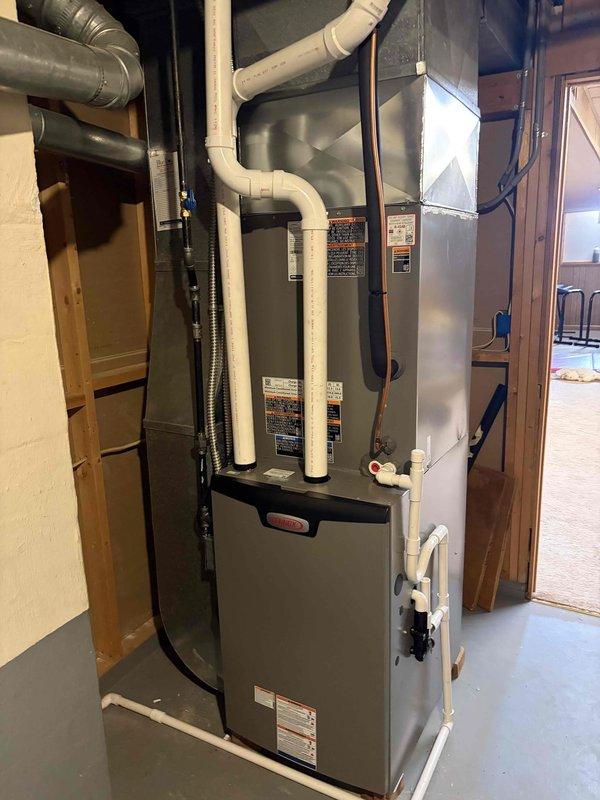 Completed installation of a new 90% efficiency furnace and air conditioning system in residential basement utility area. New gray metal furnace unit was properly positioned and secured, with all PVC venting pipes, electrical conduit, and ductwork connections installed per manufacturer specifications and local code requirements. System was tested and verified operational upon completion.