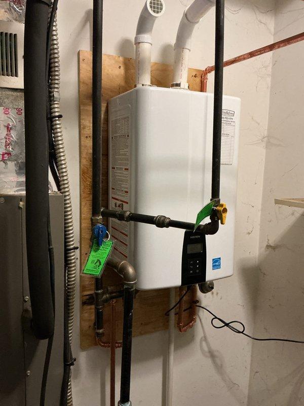 Completed professional installation of a Navien tankless water heater system in a basement utility area. The installation included mounting the unit on a plywood backing board, connecting copper supply and return lines with shutoff valves, and installing dual PVC venting pipes through the ceiling. All plumbing connections were properly fitted with appropriate valves and fittings, and the system was tested for proper operation. The installation meets manufacturer specifications and energy efficiency standards as indicated by Energy Star certification.