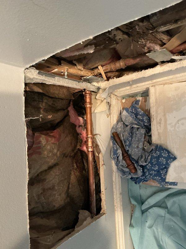 Responded to a return visit for a previously repaired leaking pipe that had failed, likely due to freezing conditions. Opened interior wall and ceiling to access the affected copper plumbing, revealing deteriorated insulation and water damage in the wall cavity. Assessed the failed repair site, documented the condition of the copper piping showing varying degrees of oxidation, and prepared the area for proper re-repair of the leaking section.