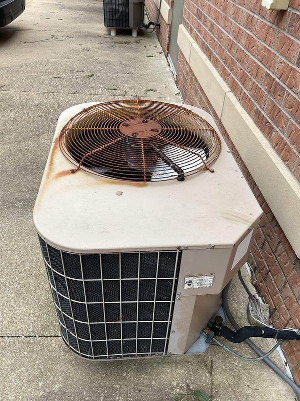 Completed comprehensive AC tune-up on outdoor condensing unit showing visible age and weathering, including rust staining around fan assembly area. Performed standard preventive maintenance procedures including inspection of all components, cleaning of condenser coils, verification of proper refrigerant levels, testing of electrical connections, and evaluation of fan motor operation. Unit operational upon completion with recommendations provided for monitoring rust progression on top panel.