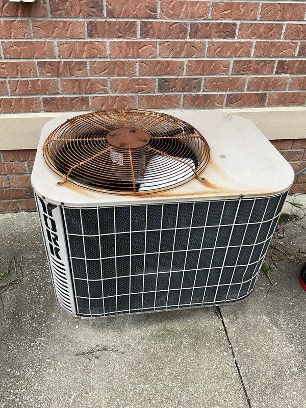 Completed comprehensive AC tune-up on outdoor condensing unit showing visible age and weathering, including rust staining around fan assembly area. Performed standard preventive maintenance procedures including inspection of all components, cleaning of condenser coils, verification of proper refrigerant levels, testing of electrical connections, and evaluation of fan motor operation. Unit operational upon completion with recommendations provided for monitoring rust progression on top panel.