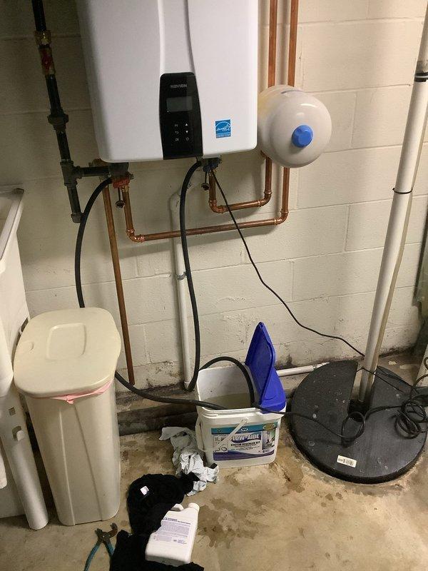Performed scheduled maintenance flush on Navien tankless water heater unit located in basement utility area. Isolated unit from water supply, connected service hoses, and circulated descaling solution through heat exchanger to remove mineral buildup and calcium deposits. Flushed system thoroughly with clean water to clear all descaling agent residue. Inspected copper supply and return piping connections, expansion tank, and all associated valves for proper operation and signs of leakage. Verified unit operation upon completion, confirmed proper flow rates, and ensured digital control panel displayed normal operating parameters. System returned to service with optimal performance restored.