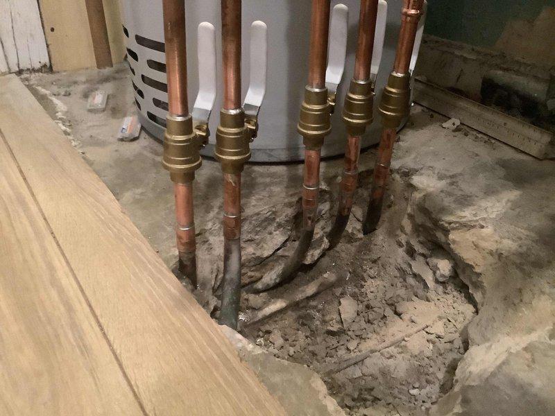 Repaired two leaking 1/2" copper supply lines on the supply side of radiant heating manifold. Jackhammered concrete flooring to expose underground copper risers that were leaking due to direct contact with concrete without proper insulation or pipe wrapping. Brazed new copper risers onto existing radiant lines and rebuilt manifold connections with brass compression fittings. Corrosion damage was caused by abrasive contact between unprotected copper piping and concrete during original installation. Successfully completed repairs without extending work into hallway area. Water heater remained in place as access was sufficient from current location. Patched concrete flooring after plumbing work was completed.