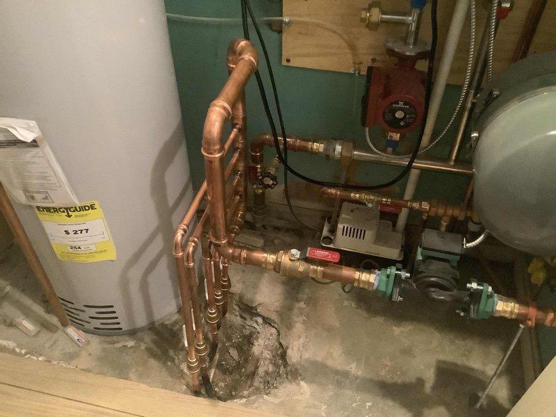 Repaired two leaking 1/2" copper supply lines on the supply side of radiant heating manifold. Jackhammered concrete flooring to expose underground copper risers that were leaking due to direct contact with concrete without proper insulation or pipe wrapping. Brazed new copper risers onto existing radiant lines and rebuilt manifold connections with brass compression fittings. Corrosion damage was caused by abrasive contact between unprotected copper piping and concrete during original installation. Successfully completed repairs without extending work into hallway area. Water heater remained in place as access was sufficient from current location. Patched concrete flooring after plumbing work was completed.
