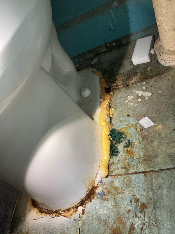 Responded to service call for strong odor emanating from toilet. Upon inspection, discovered extensive deterioration in toilet tank interior with significant rust accumulation on metal components and heavy mineral deposit buildup throughout. Water supply line and internal tank mechanisms showed signs of age-related wear. Examined toilet base and surrounding floor area, noting degraded wax ring seal evidenced by discolored expanding foam material and moisture damage to flooring. Documented rust staining on floor surfaces and compromised seal integrity at toilet-to-floor connection point, which was identified as primary source of odor complaint. Assessed overall fixture condition revealing advanced deterioration requiring attention to internal tank components and base seal replacement to resolve sanitation concerns and eliminate odor issue.