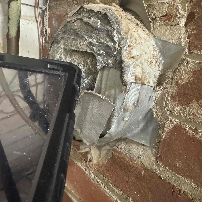 Responded to service call for furnace making abnormal noise during and after heating cycles. Upon inspection, discovered severely deteriorated dryer vent ductwork penetrating through exterior brick wall with extensive damage to metal housing and significant lint accumulation inside the vent system. The ductwork insulation showed heavy degradation with multiple tears and layers separated from original position. Documented conditions with photos showing compromised vent integrity, torn metal fragments, and buildup of debris that could potentially impact HVAC system operation and create safety concerns. Assessed whether issue was related to scheduled maintenance appointment to determine appropriate next steps for repair.