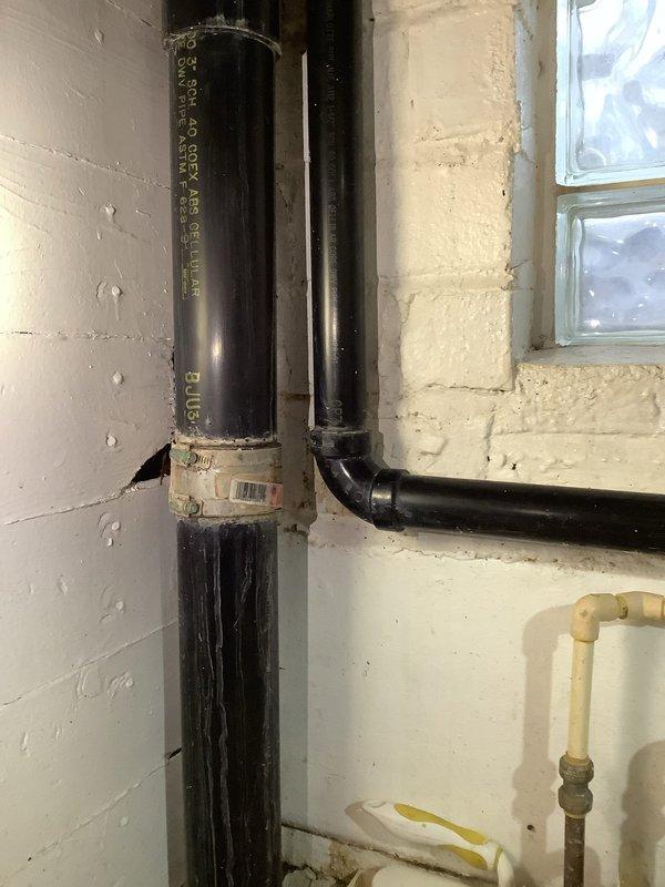 Conducted main line repair estimate for stack replacement in basement utility area. Assessed existing vertical drainage pipes running along cinder block wall and evaluated P-trap configuration beneath sink fixture. Documented current plumbing infrastructure conditions including aged black drain pipes, mounting hardware, and wall-mounted drain assembly showing signs of moisture exposure and typical wear. Technician to return following completion of restoration company's work to finalize stack replacement installation.