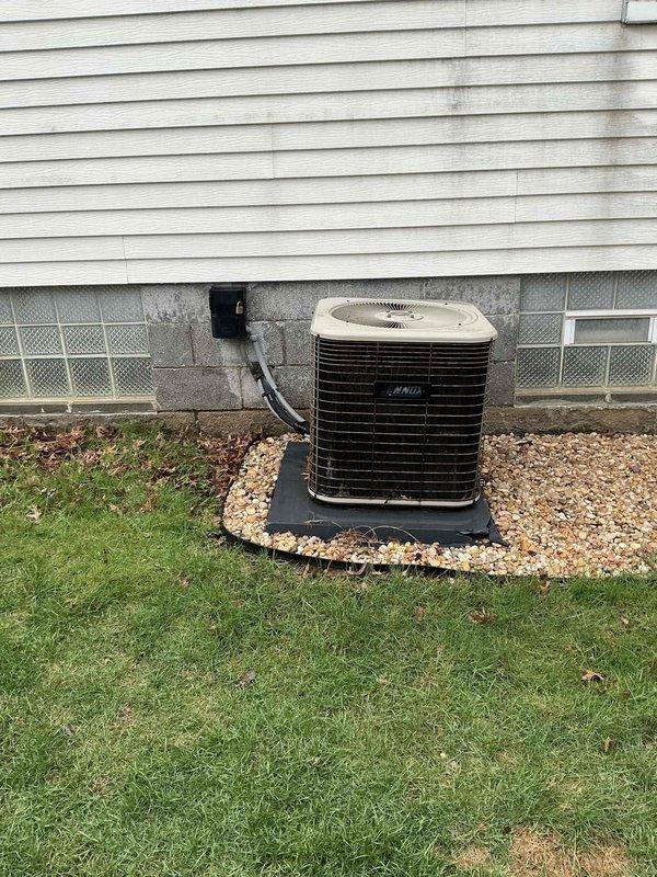 Conducted comprehensive evaluation of 30-year-old residential HVAC system including outdoor condensing unit and indoor air handler for replacement estimate. Assessed existing equipment condition, documented current installation configuration with exterior unit positioned on rubber pad with stone surround and glass block foundation windows, and inspected basement air handler with associated ductwork, copper refrigerant lines, and filter drier components to provide accurate replacement recommendations.