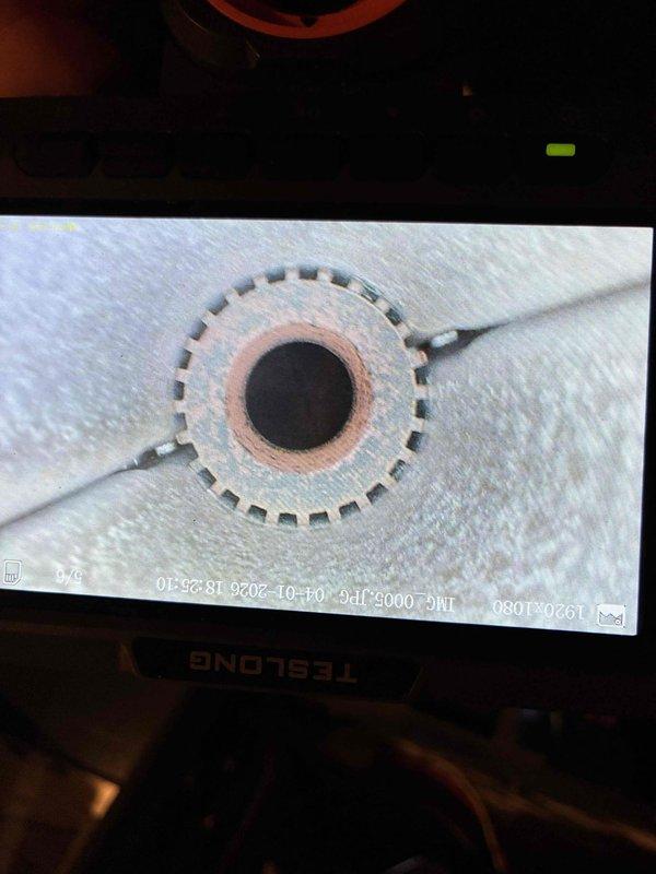 Responded to furnace tune-up request and performed comprehensive heating system inspection. Utilized TESLONG borescope camera to conduct detailed internal examination of heat exchanger, capturing digital images of burner assembly and flame ports. Visual inspection revealed heat exchanger interior with circular burner orifice showing normal copper-colored flame ring pattern and evenly-spaced port openings arranged in gear-like configuration, indicating proper combustion characteristics and no visible cracks or deterioration in exchanger material.