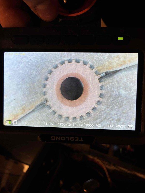 Responded to furnace tune-up request and performed comprehensive heating system inspection. Utilized TESLONG borescope camera to conduct detailed internal examination of heat exchanger, capturing digital images of burner assembly and flame ports. Visual inspection revealed heat exchanger interior with circular burner orifice showing normal copper-colored flame ring pattern and evenly-spaced port openings arranged in gear-like configuration, indicating proper combustion characteristics and no visible cracks or deterioration in exchanger material.