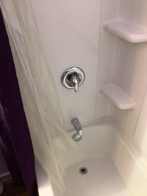 Completed full tub-to-shower conversion by removing existing bathtub and surround walls. Jackhammered concrete floor to expose and upsize existing water supply piping. Removed toilet for access and installed new toilet flange after tying into main drain line with new piping. Poured rough concrete patch over new plumbing infrastructure. Set new fiberglass shower base on mortar bed to ensure proper leveling and installed matching wall surround panels. Installed new single-handle shower valve with chrome trim kit and chrome tub spout. Mounted horizontal grab bar in shower enclosure for safety. All plumbing connections tested and verified operational.
