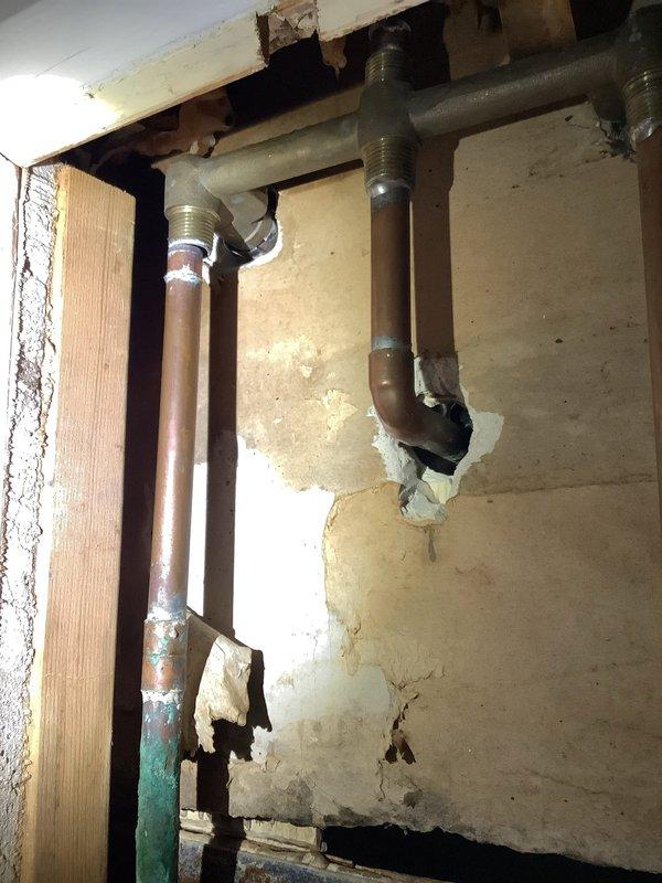 Responded to emergency call for burst pipe in wall causing flooding in crawl space. Upon arrival, found malfunctioning shut-off valve requiring main water supply to be shut off to entire residence. Accessed plumbing infrastructure through wall opening in basement area, exposing copper pipes with brass fittings connected to steel supply lines. Assessed damaged section and surrounding pipe connections within wooden frame structure. Documented existing conditions including compromised piping, water damage to surrounding materials, and configuration of vertical and horizontal supply runs. Verified proper shutdown of water supply to prevent further flooding and prepared area for necessary repairs.