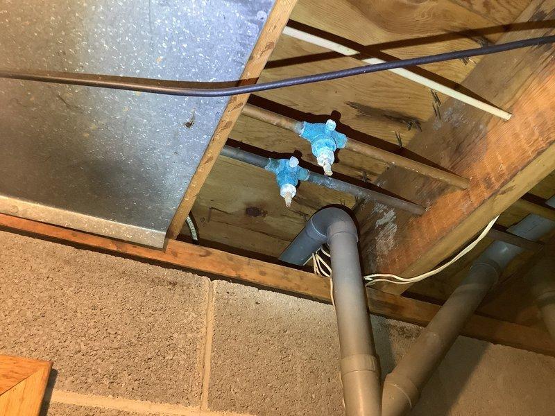 Responded to emergency call for burst pipe in wall causing flooding in crawl space. Upon arrival, found malfunctioning shut-off valve requiring main water supply to be shut off to entire residence. Accessed plumbing infrastructure through wall opening in basement area, exposing copper pipes with brass fittings connected to steel supply lines. Assessed damaged section and surrounding pipe connections within wooden frame structure. Documented existing conditions including compromised piping, water damage to surrounding materials, and configuration of vertical and horizontal supply runs. Verified proper shutdown of water supply to prevent further flooding and prepared area for necessary repairs.