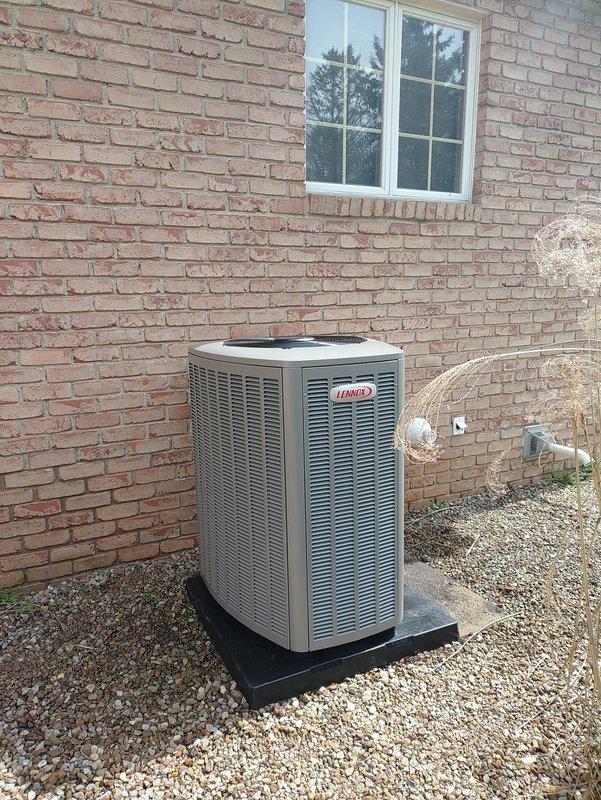 Completed full system installation of a Lennox 90% efficiency air conditioning unit at residential property. New condenser unit was positioned on black platform pad with gravel base against exterior brick wall, with proper clearances maintained for airflow and service access. All refrigerant lines, electrical connections, and condensate drainage were installed to manufacturer specifications. System was pressure tested, charged with refrigerant, and verified operational with digital gauges confirming proper temperatures and pressures across the system.