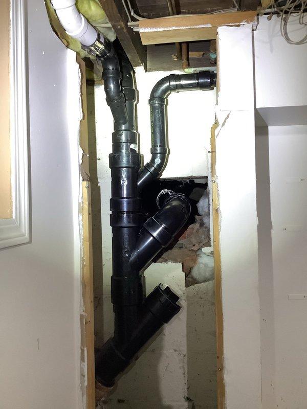 Completed extensive ABS drain pipe replacement due to broken fitting in main drainage stack. Cut out and removed compromised hub-to-hub fittings from basement through first floor offset, requiring access through kitchen cabinet back panel and basement drywall removal. Accessed crawl space to cut and remove 4" drain pipe section. Rebuilt entire drainage assembly maintaining original configuration and orientation to properly connect with existing plumbing infrastructure. Replacement parts were ordered and received prior to completion of repair work. Additionally scheduled follow-up appointment to replace expansion tank, estimated one hour duration.
