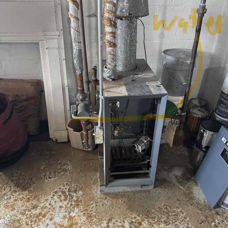 Responded to service call for 20-year-old boiler that became inoperative after basement flooding. Upon inspection, found significant water damage to heating unit with visible moisture staining throughout mechanical room floor and equipment base. Boiler had been submerged during flood event, compromising internal components including burner assembly, controls, and electrical systems. Documented extensive water damage with photographs showing mineral deposits on concrete floor, exposed internal mechanisms with front panel removed for assessment, and affected piping systems. Given the age of the unit and extent of water intrusion into critical components, advised that boiler replacement would be necessary as flood damage to gas-fired heating equipment typically affects multiple systems beyond economical repair.