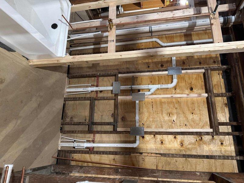 Met with inspector at 8am as scheduled to review plumbing installation in unfinished utility and attic spaces. Inspection covered white PVC drainage system with multiple branch configurations, T-joints, and elbows secured to wooden framing with gray plastic mounting brackets. Vertical and horizontal pipe runs were examined throughout both levels, including connections between tiled utility area and upper floor rough-in. All plumbing infrastructure was presented for code compliance verification and approval.
