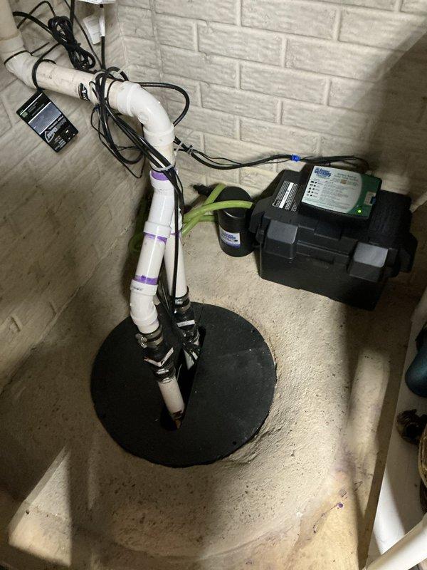 Responded to emergency service call for failed primary sump pump with activated backup battery system. Upon arrival, conducted thorough inspection of existing sump pump installation and determined main pump had reached end of service life and required immediate replacement. Removed failed primary sump pump unit from basin and cleared debris from sump pit to ensure proper operation of new equipment.

Installed new residential-grade sump pump in existing basin with appropriate discharge piping configuration. Connected white PVC discharge line using proper primer and cement techniques, ensuring all joints were secure and leak-free. Verified proper float switch operation and pump activation at correct water levels. Secured all electrical wiring with zip ties and organized cables along existing pipe runs to maintain clean installation appearance.

Tested backup battery sump pump system to confirm operational readiness and verified battery charge level was adequate for extended power outage 