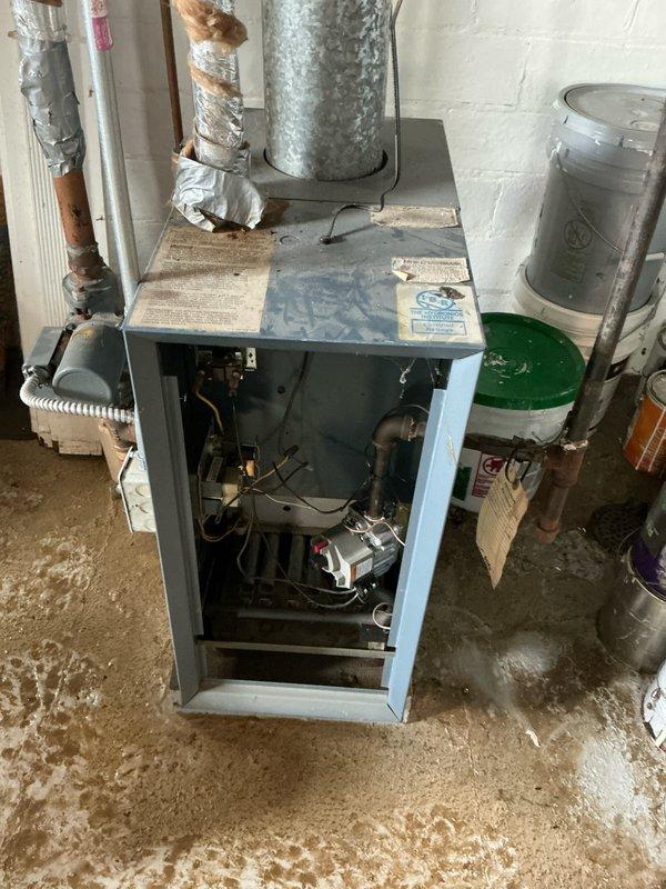 Performed comprehensive estimate for boiler and hot water tank replacement in basement utility area. Unit had experienced water damage with standing water present around equipment. Documented existing heating system configuration including light blue/gray boiler unit with exposed internal components, metallic flue pipe with visible condensation, copper piping with silver insulation, and white PVC connections. Assessed HVAC ductwork, overhead piping systems, and overall installation conditions in cinder block basement environment to provide accurate replacement recommendations.