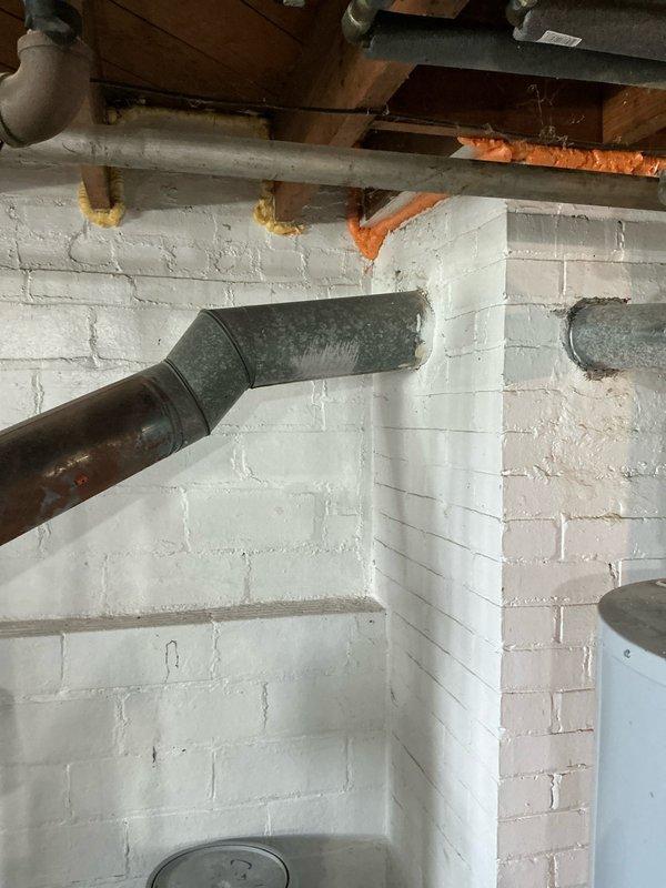 Performed comprehensive estimate for boiler and hot water tank replacement in basement utility area. Unit had experienced water damage with standing water present around equipment. Documented existing heating system configuration including light blue/gray boiler unit with exposed internal components, metallic flue pipe with visible condensation, copper piping with silver insulation, and white PVC connections. Assessed HVAC ductwork, overhead piping systems, and overall installation conditions in cinder block basement environment to provide accurate replacement recommendations.