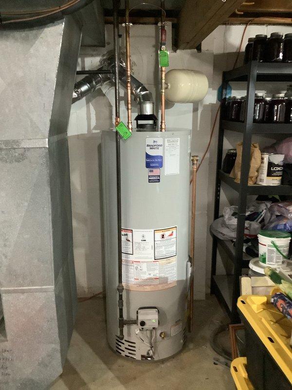 Removed existing AO Smith water heater and installed new Bradford White residential water heater unit in basement utility area. Brought installation up to current code compliance by installing new shut-off valves for both water supply and gas lines, and added proper bonding connections to the unit. Connected copper supply piping with brass fittings, installed cream-colored expansion tank, and attached emergency shut-off identification tags to valves for safety compliance. All plumbing connections tested and verified operational upon completion.