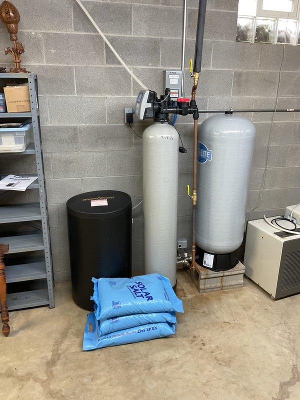 Completed salt delivery service for water softener system at residential property. Delivered three bags of water softener salt from warehouse inventory to basement utility area and placed them in front of existing Water-Right Sanitizer Plus dual-tank water treatment system. Verified system control panel displayed proper water hardness setting of 21 grains and confirmed adequate salt supply for continued operation of the softening equipment.