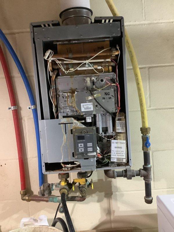 Performed routine flush and maintenance service on gas-fired tankless water heater unit. Removed front access panel to expose internal components, heat exchanger, and control systems. Isolated water supply using existing shut-off valves on inlet and outlet lines, then connected flushing equipment to service ports. Circulated descaling solution through heat exchanger to remove mineral deposits and scale buildup. Inspected gas supply line connections, yellow-handled shut-off valves, and flexible gas line for proper operation and potential leaks. Examined corroded brass fittings and shut-off valves showing significant oxidation, mineral deposits, and green patina buildup, indicating age-related deterioration and moisture exposure. Checked PEX water supply lines, exhaust venting system with PVC piping, burner assembly, copper tubing connections, and electrical wiring harnesses for proper condition. Verified control board operation and all internal components functioning correctly. Flushed 