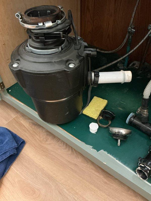 Re-plumbed kitchen sink following new countertop installation, including reinstallation of garbage disposal unit and all associated drain assemblies. Disassembled existing disposal and drain components, cleaned and inspected all fittings and connections, then reassembled the complete under-sink plumbing system with proper alignment to accommodate the new counter configuration.