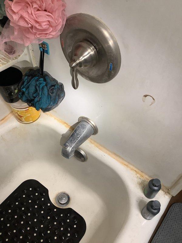 Responded to water leak emergency where shower faucet was allowing water to run down the back of the fixture into drop ceiling, causing water accumulation on basement floor below. Inspected plumbing access point beneath bathroom revealing mix of PVC and aged copper piping with visible corrosion, assessed bathtub fixtures showing mineral buildup and water spotting, and documented compromised seal at faucet mounting point requiring repair to prevent further water intrusion and structural damage.