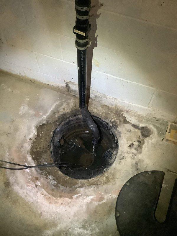 Responded to emergency service call for sump pump system causing water flooding in yard and adjacent property. Inspected basement sump pump installation and identified discharge system failure allowing water to overflow. Assessed exterior drainage configuration including downspout connections and PVC discharge piping extending from foundation. Documented existing conditions showing weathered concrete floor with mineral deposits and moisture staining around sump pit, standing water in basin, and compromised discharge line routing. Evaluated exterior discharge terminus where flexible ribbed piping connected to PVC elbow assembly was directing water improperly, contributing to yard flooding. Provided estimates for kitchen and bathroom faucet replacements as requested. Assessed dehumidifier unit for operational issues per homeowner request.