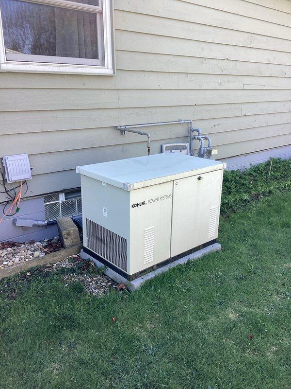 Performed comprehensive maintenance on Kohler residential backup generator system including inspection of all external components, conduit connections, and mounting hardware. Generator found in good operating condition with proper ventilation and secure installation on concrete pad. Investigated reported flickering lights throughout house and weak power issues in shed; inspected main electrical panel, branch circuits, and outdoor wiring runs. Examined exterior lighting circuits and conduit routing along foundation as requested. Verified all generator transfer switch connections and tested automatic startup functionality. Documented equipment condition with photographs showing generator placement, electrical connections, and associated exterior components including meter box and conduit pathways.