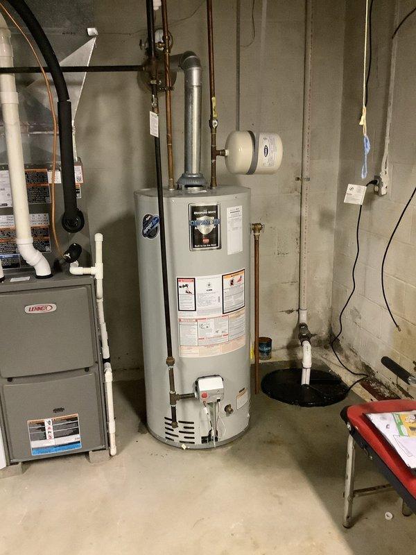 Responded to a water leak in basement originating from the potable water expansion tank. Upon arrival, found a Flexcon water expansion tank with a minor leak at the connection point, causing spray and moisture on surrounding walls and floor. Inspected the white cylindrical expansion tank mounted in the utility area near the water heater and furnace system. The leak was contained to light spray without significant pooling. Assessed copper piping connections to the expansion tank and evaluated the overall condition of the unit, which showed signs of age with visible discoloration and staining on the exterior surface. Documented the leak location at the blue valve assembly connection point on the tank. The expansion tank was positioned horizontally in the basement utility room alongside the main water heater and HVAC equipment.
