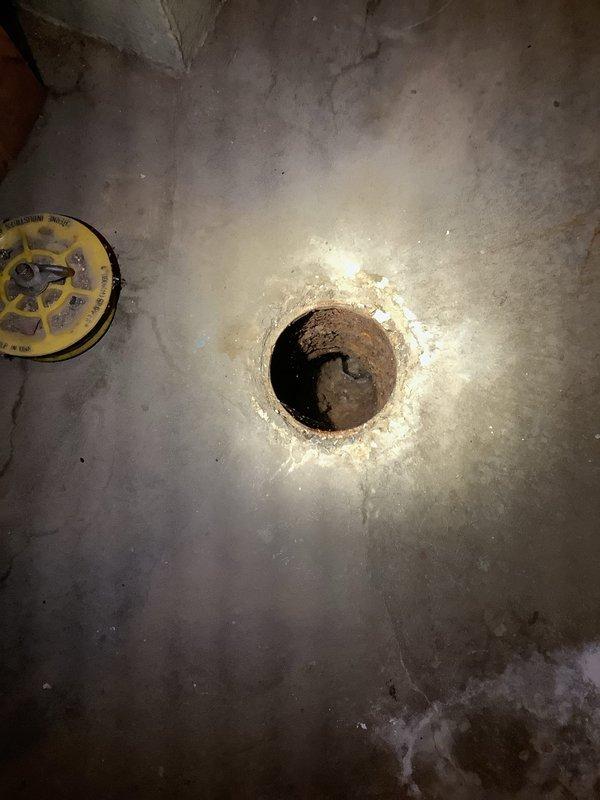 Responded to basement drainage issue where water was backing up through floor drain, preventing use of washing machine. Upon arrival, located main floor drain access point in basement with visible signs of chronic backup and water damage to surrounding concrete. 

Removed corroded drain cover and inspected drain assembly. Found severely deteriorated trap and drain line with significant rust accumulation and mineral buildup restricting water flow. Standing water in line confirmed blockage was causing backup into basement when washing machine discharged.

Cleared obstruction from main drain line using mechanical cable auger. Removed accumulated debris, soap residue, and sediment from trap assembly. Flushed line thoroughly to restore proper drainage and verify water flow. Tested system by running water to confirm backup issue resolved and drainage functioning correctly. Customer advised that washing machine can now be operated normally without water returning through floor drain.