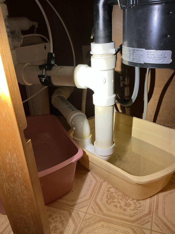 # Clogged Kitchen Sink - Drain Clearing Service

Responded to service call for clogged kitchen sink in 38-year-old residential property. Upon arrival, assessed the drainage system and identified blockage affecting kitchen sink discharge. 

Accessed plumbing assembly beneath sink, which included white PVC drain piping with P-trap configuration connected to garbage disposal unit via black rubber coupling. Inspected vertical drain stack and horizontal waste line for obstruction points. Examined basement plumbing infrastructure where kitchen drain line connects to main waste stack, noting PVC piping routing through floor joists.

Performed drain clearing procedures to remove blockage and restore proper water flow. Tested drainage system by running water through sink and garbage disposal to verify complete clearance and proper discharge rate. Confirmed P-trap maintained adequate water seal and all connections remained secure with no leaks present.

System restored to full operational status
