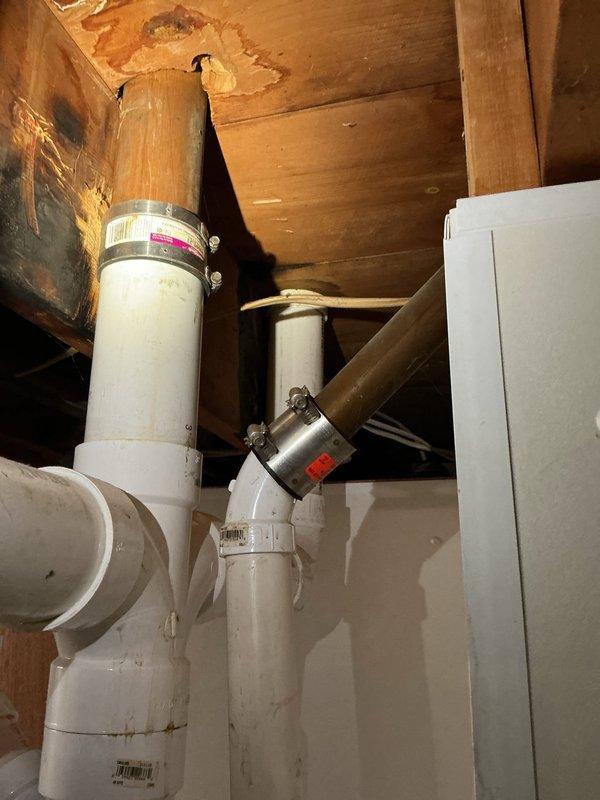 Responded to service call for leaking stack at base. Upon inspection, discovered compromised seal at floor drain connection where main stack meets basement floor. Removed deteriorated drain covers and assessed PVC stack assembly. Identified moisture damage in overhead framing and staining on ceiling materials from previous leak exposure. Documented existing plumbing configuration including vertical stack, multiple branch connections with hose clamps, and floor drain fitting with brass threading. Photographed conditions for repair assessment and customer records.