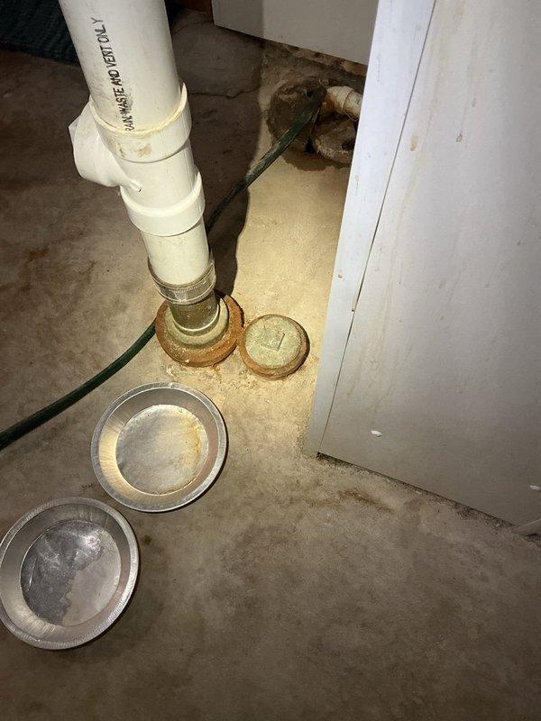 Responded to service call for leaking stack at base. Upon inspection, discovered compromised seal at floor drain connection where main stack meets basement floor. Removed deteriorated drain covers and assessed PVC stack assembly. Identified moisture damage in overhead framing and staining on ceiling materials from previous leak exposure. Documented existing plumbing configuration including vertical stack, multiple branch connections with hose clamps, and floor drain fitting with brass threading. Photographed conditions for repair assessment and customer records.