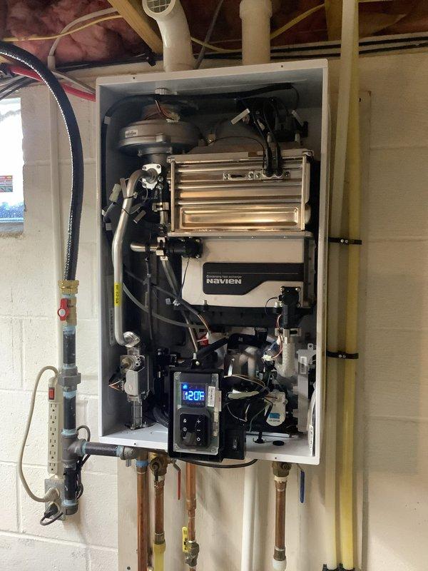 Responded to service call for Navien tankless water heater experiencing intermittent temperature fluctuations and unusual noise during operation. Upon inspection, opened access panel and examined internal components including heat exchanger, blower assembly, and control board. Identified potential issue with flow sensor or gas valve solenoid causing system to cycle improperly. Inspected all wiring connections, gas line connections with flexible connector and shut-off valve, and copper water supply lines with brass fittings. Verified digital control panel displaying 120°F setpoint. Documented internal component condition with photos for reference. Unit mounted in basement utility area with adequate ventilation and proper venting configuration.